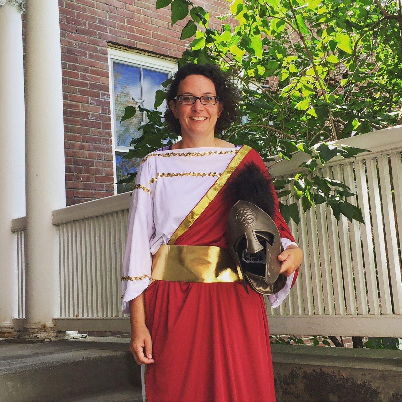 Blog Author Emily Gray dressed in her Athena costume, with a white draped tunic and red draped himation, both with gold detailing. 